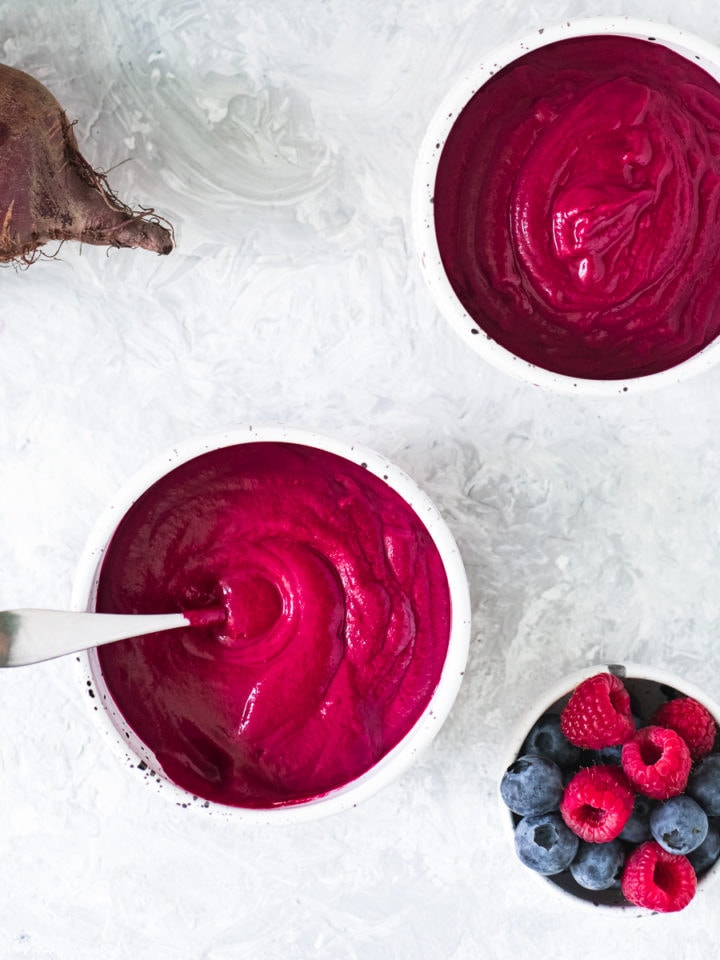 Two bowls of Cinnamon Berry Beet Smoothie freshly poured with the blender and a bowl of mixed berries sitting beside.