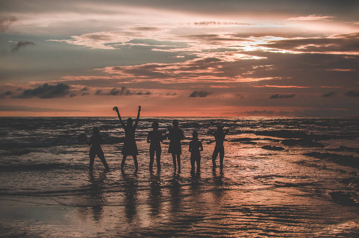 The silhouettes of six women standing in the ocean during an orange sunset communing with nature and spirit.
