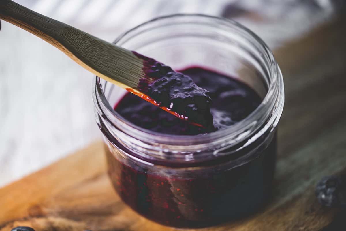 A wooden butter knife dipping into a jar of blueberry chia jam.