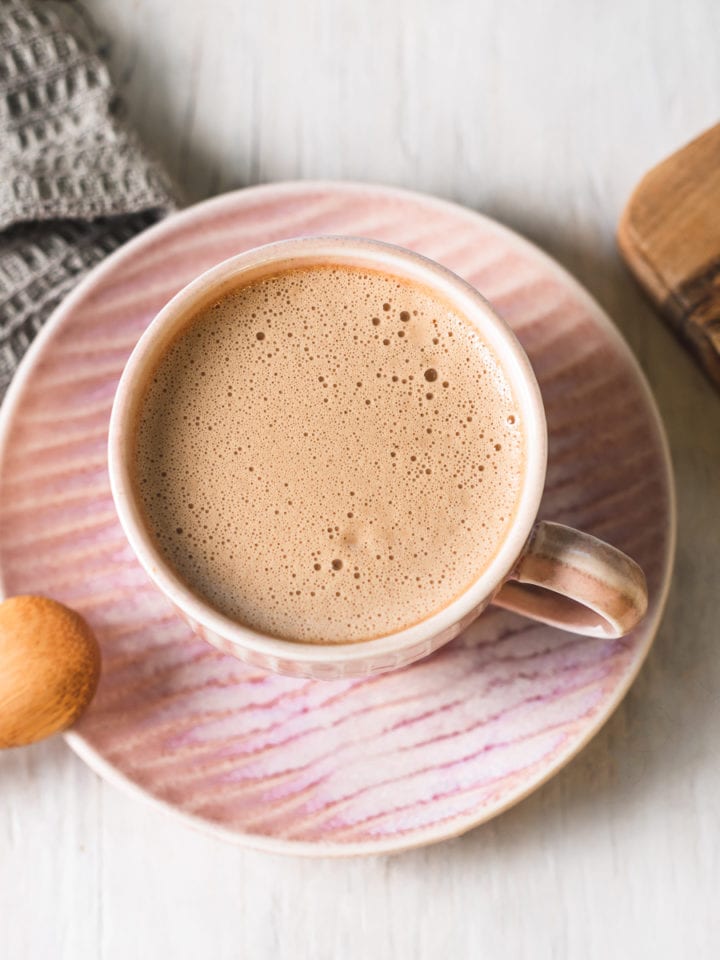 A frothy caffeine free latte in a pink tea cup on a matching plate.