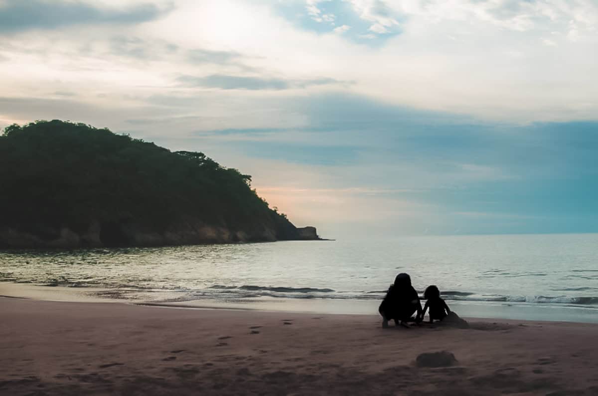 The silhouettes of a mother and child playing on sandy beach.