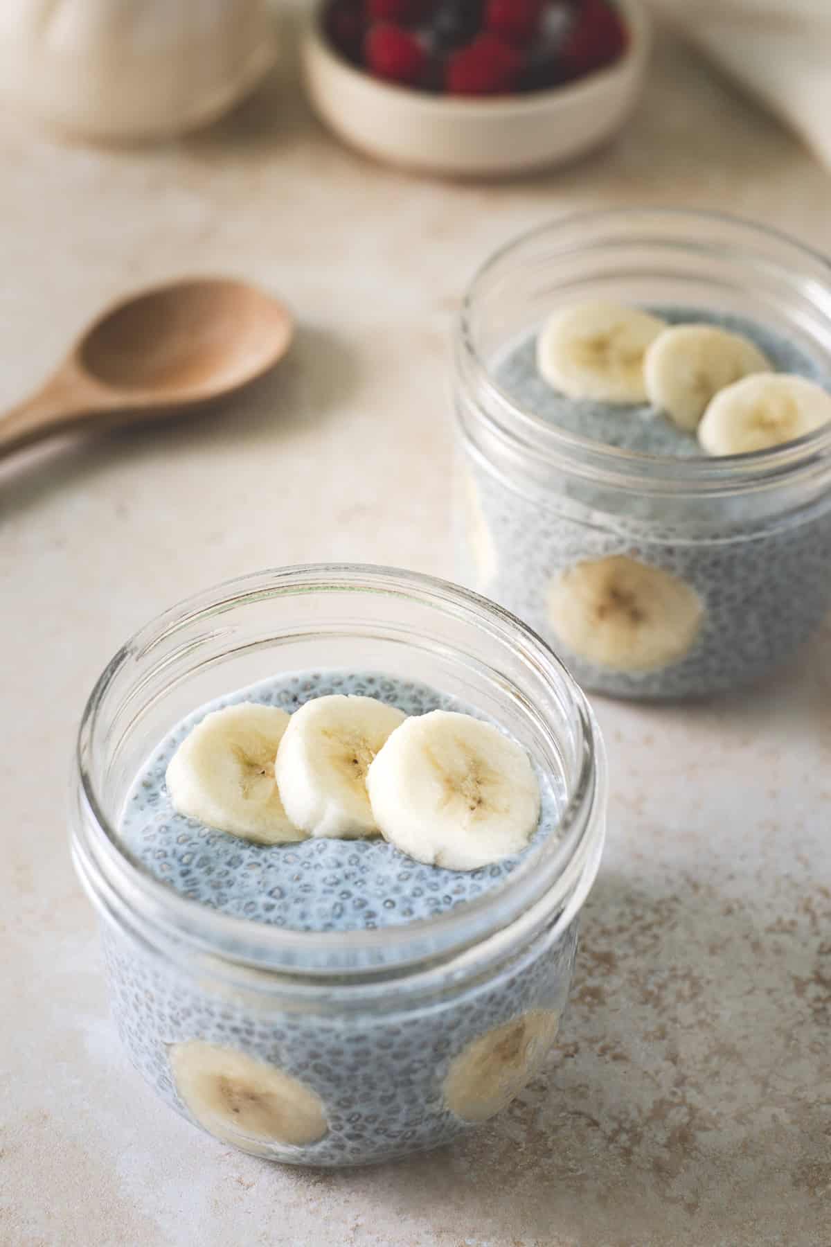 Two jars filled with blue chia seed pudding served with a jug of milk and a bowl of fresh berries.