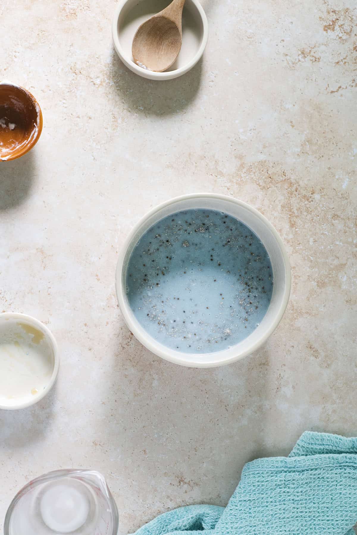 A bowl of chia seeds mixed with blue-green algae, almond milk and coconut cream with empty measuring bowls resting to the right.