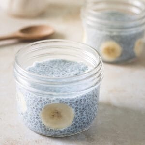 Blue chia seed pudding served in two glass jars and garnished with sliced banana.