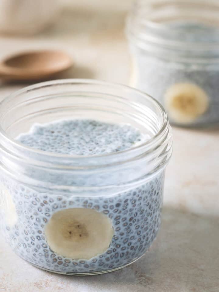 Blue chia seed pudding served in two glass jars and garnished with sliced banana.