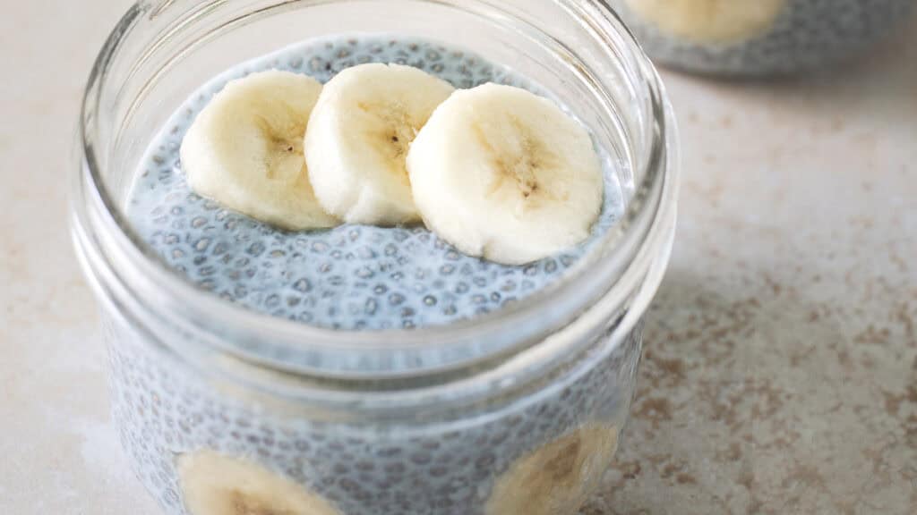 A jar of blue chia seed pudding seed topped with sliced banana.