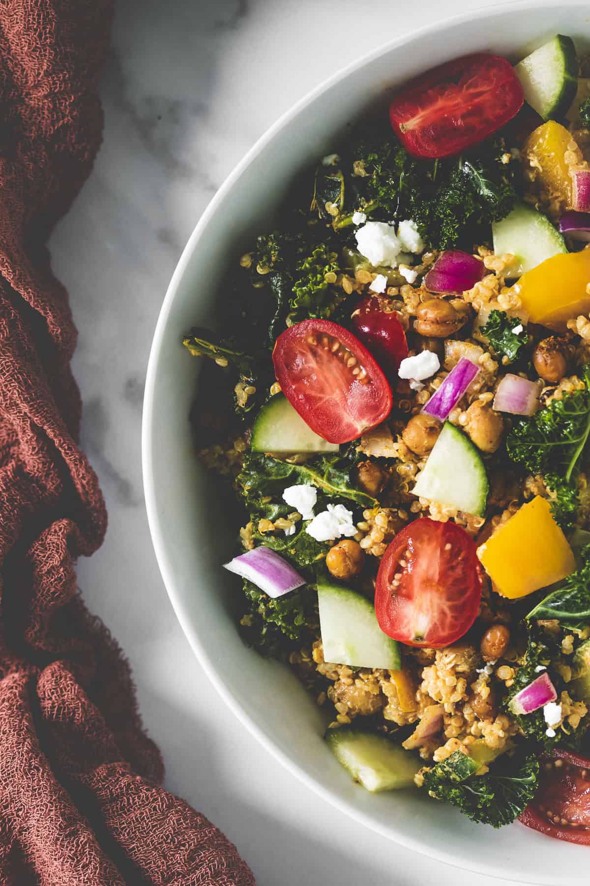 A burnt orange napkin strewn along side of a bowl of quinoa salad.