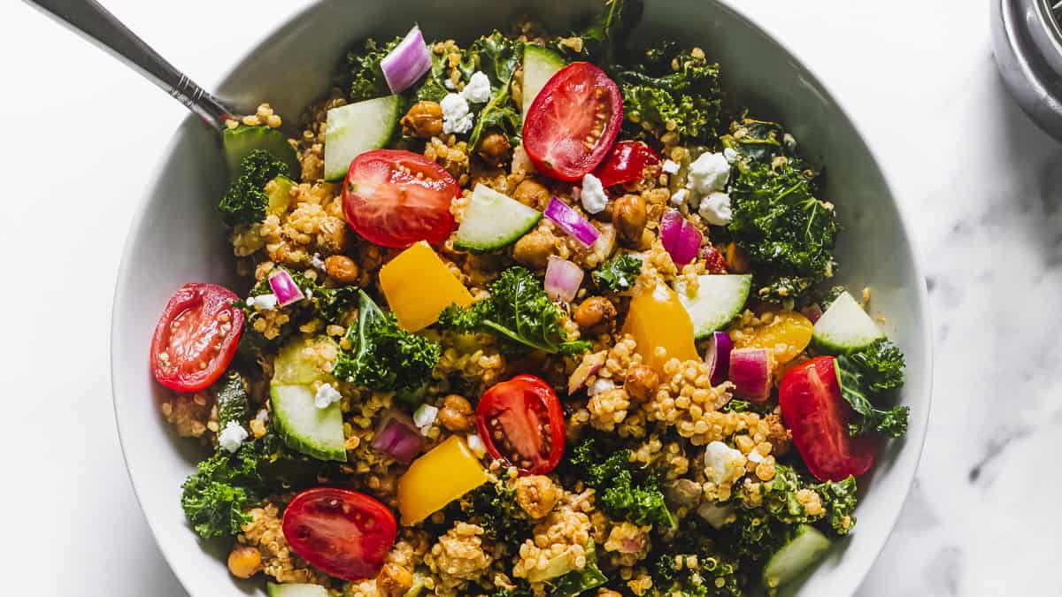 A bowl of quinoa salad with roasted chickpeas, fresh cherry tomatoes, red onion, cucumber and kale.