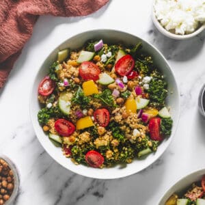 A large bowl of Quinoa Salad served on a table with fresh cucumber, dressing and chèvre.