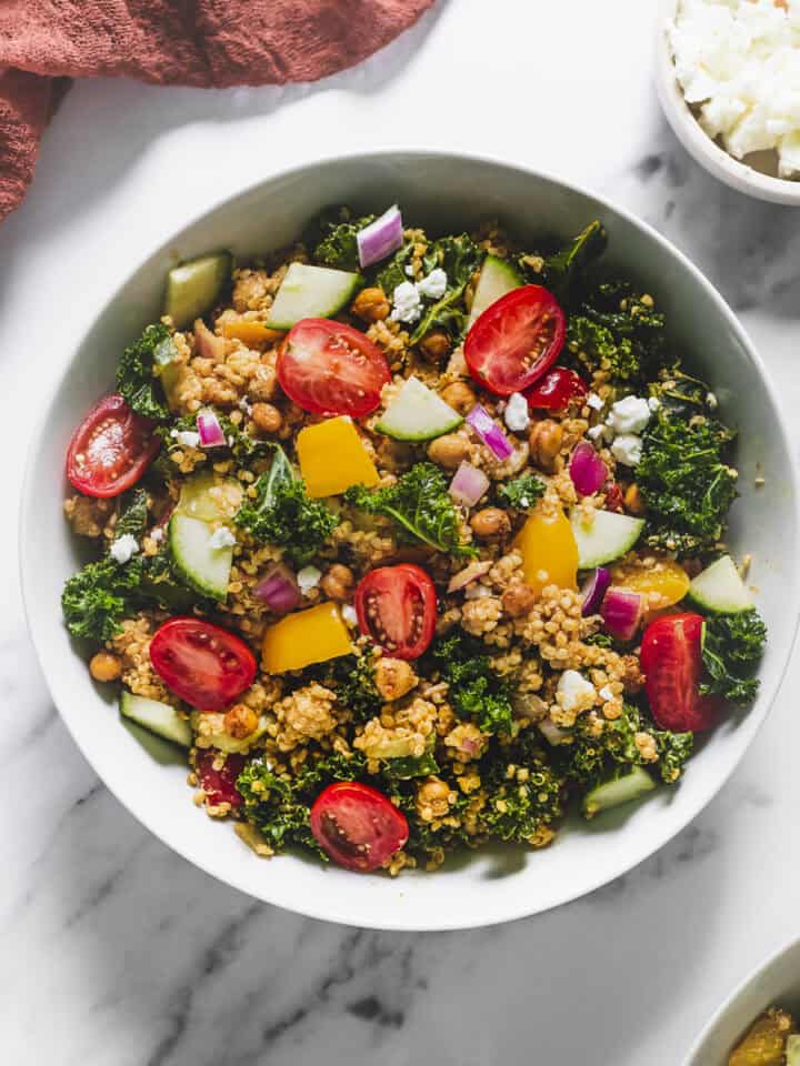 A large bowl of Quinoa Salad served on a table with fresh cucumber, dressing and chèvre.
