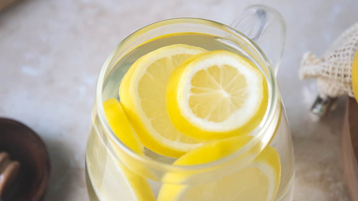 A glass mug filled with water and floating lemon slices.