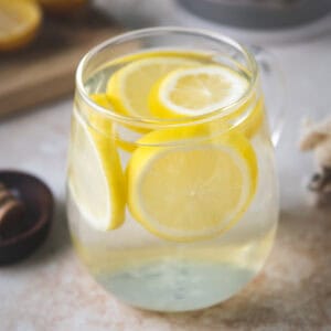 A glass mug filled with water and floating lemon rounds.