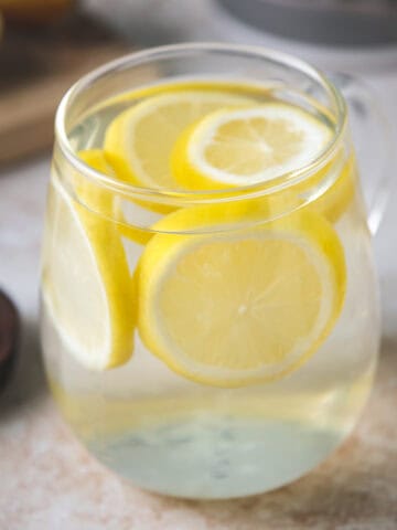 A glass mug filled with water and floating lemon rounds.