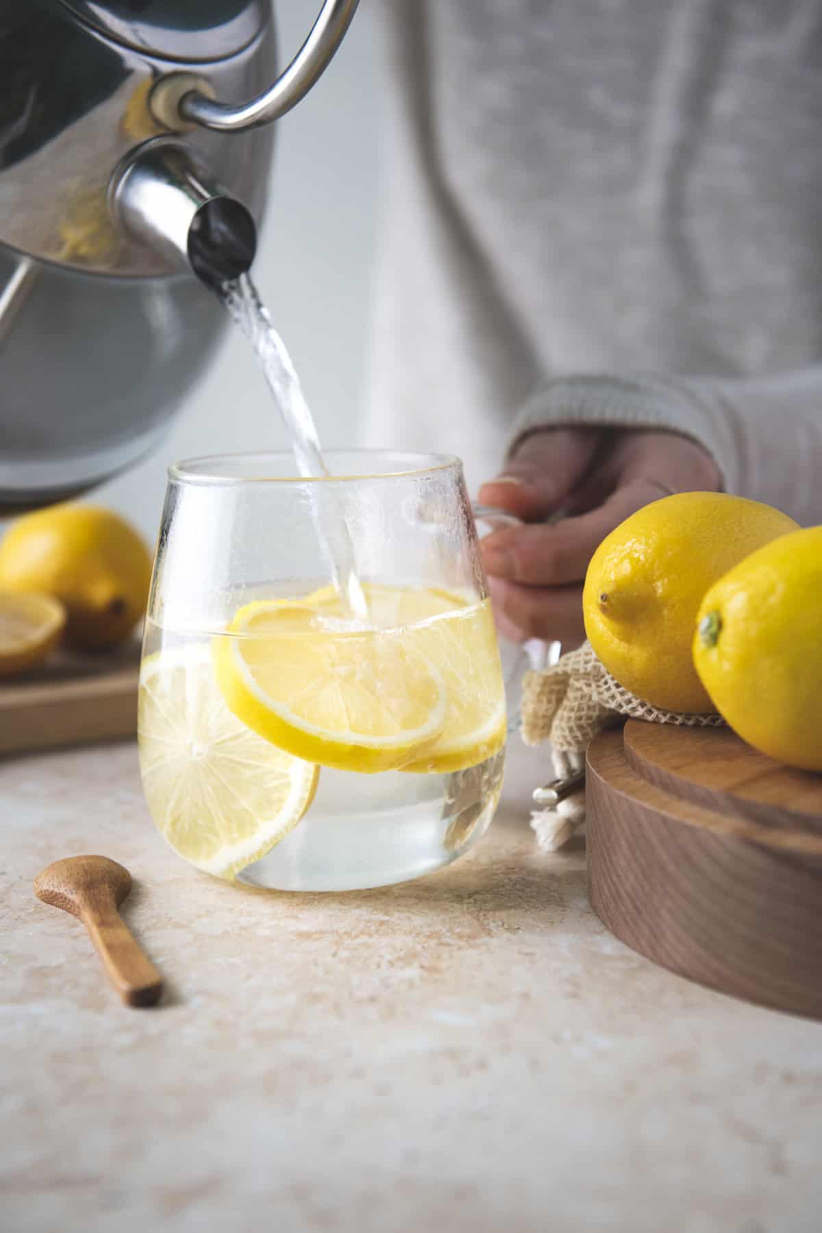 Boiling water being poured from a kettle into a glass mug with sliced lemon.